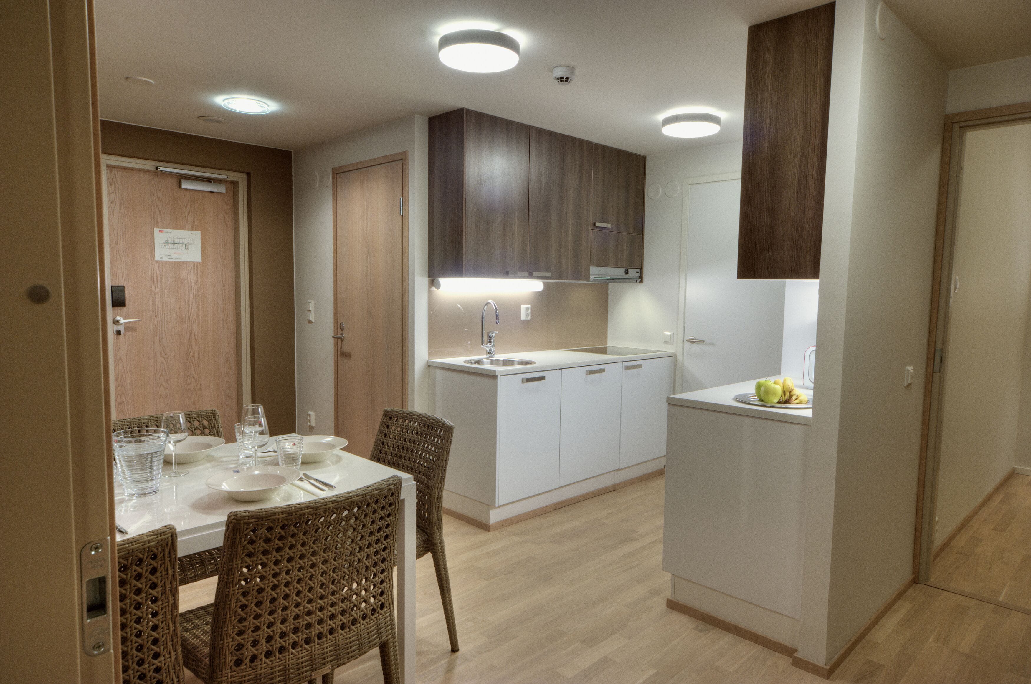 A compact kitchen with white cabinets, a built-in sink, and a dining area with wicker chairs and a table set for four.