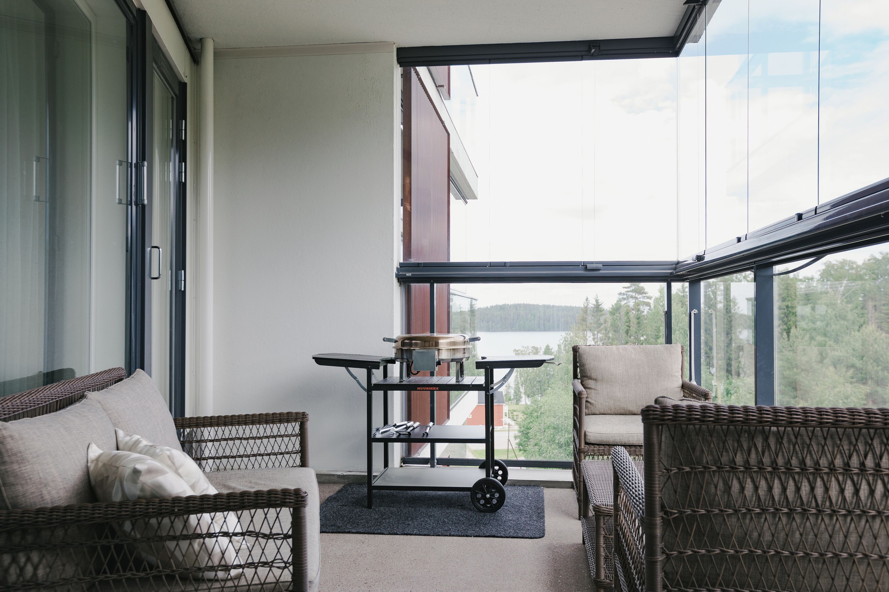 Ein Balkon mit Korbmöbeln, einem Wagen und Blick auf ein Gebäude und Bäume.