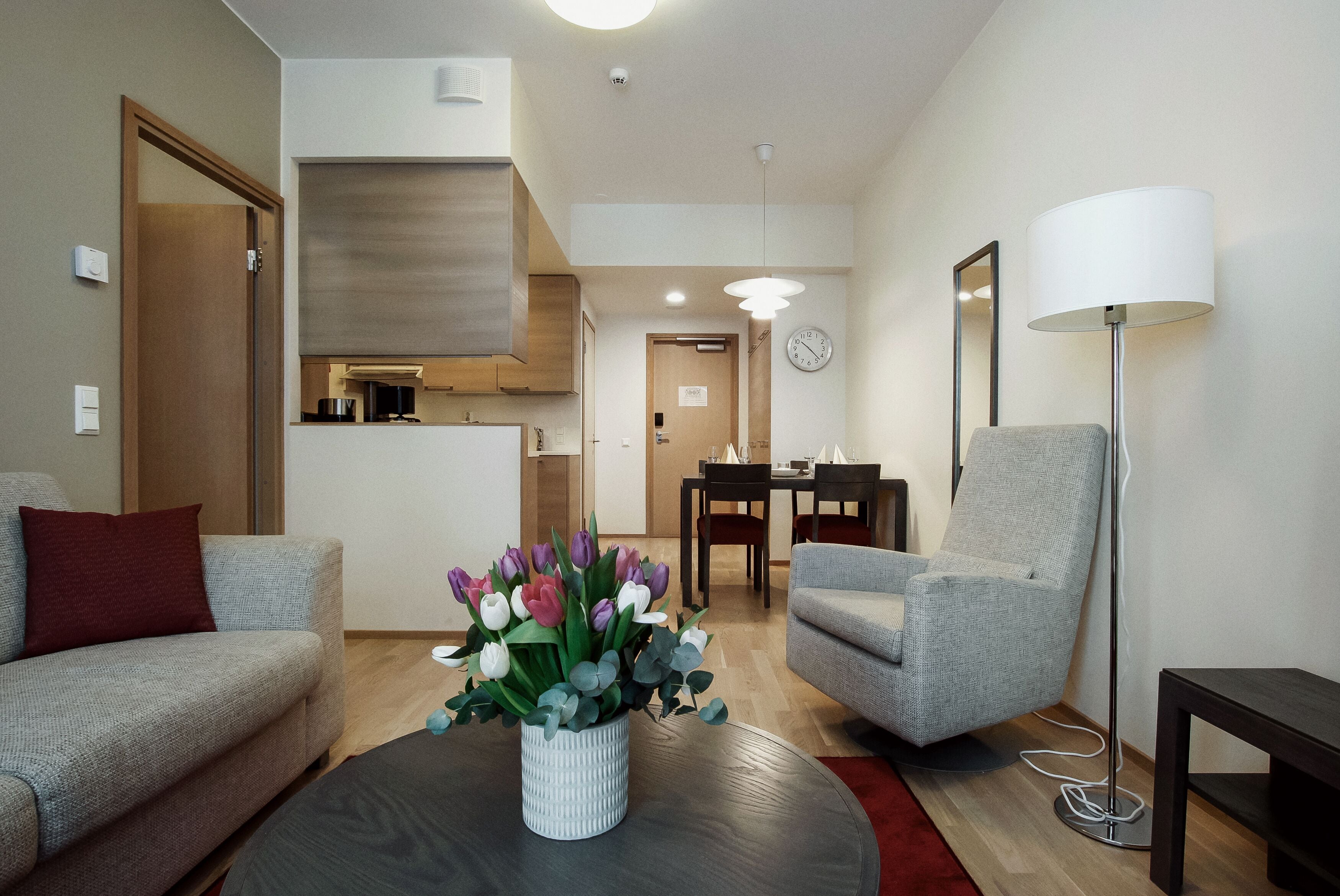 A modern living room with a sofa, armchair, and a coffee table with a flower vase.