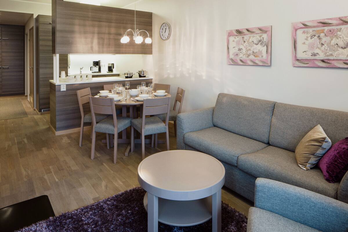 A modern living room with a grey sofa, a round coffee table, and a dining area with a wooden table and chairs.