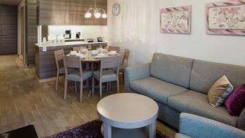 A modern living room with a grey sofa, a round coffee table, and a dining area with a wooden table and chairs.