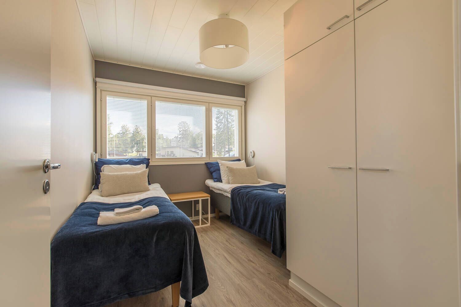A bedroom with two beds, a small table, and a wardrobe.