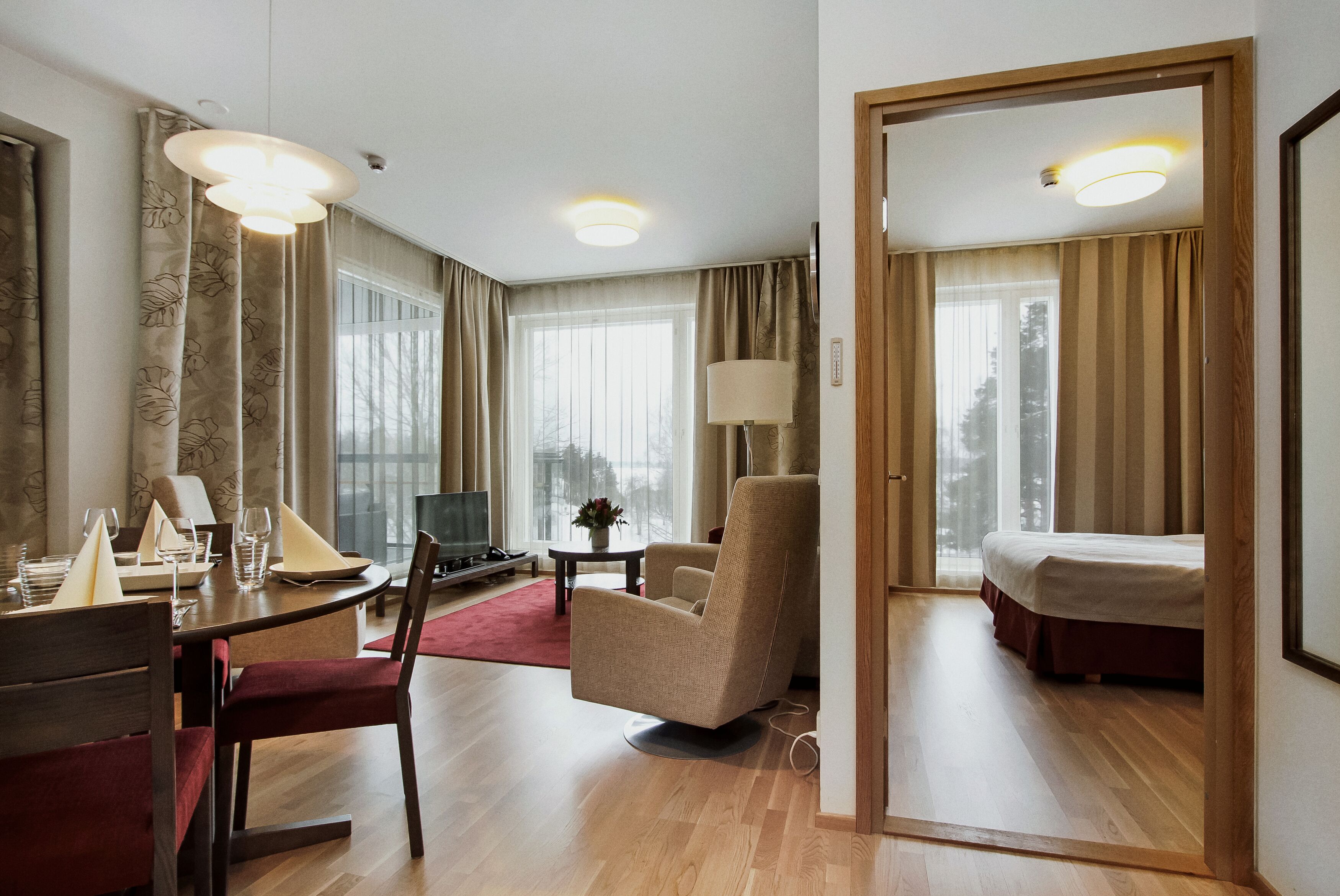 A hotel room with a dining area, a bed, and a large window with curtains.