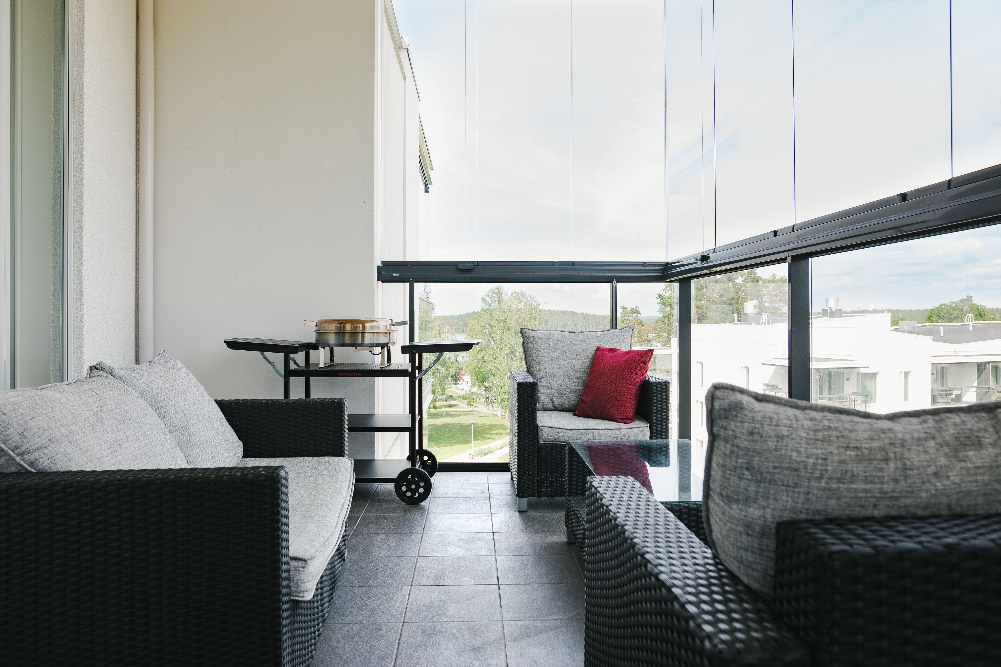 A balcony with wicker furniture, a small table with a bowl, and a view of buildings and greenery.