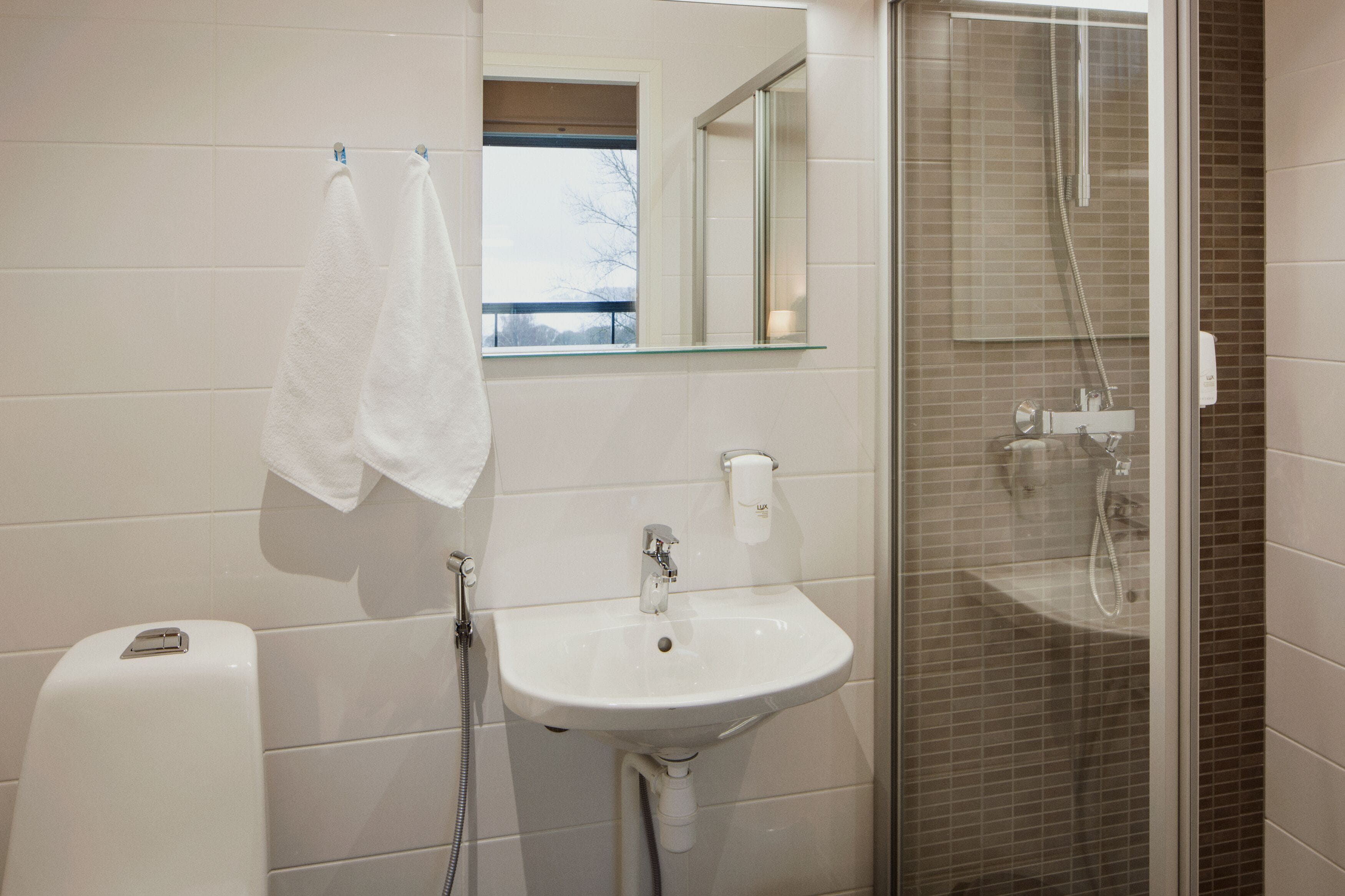 Un baño con un lavabo blanco, una mampara de cristal para la ducha y una toalla colgada en la pared.