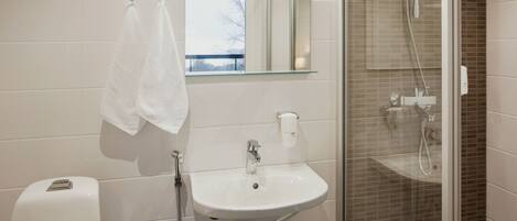 Un baño con un lavabo blanco, una mampara de cristal para la ducha y una toalla colgada en la pared.