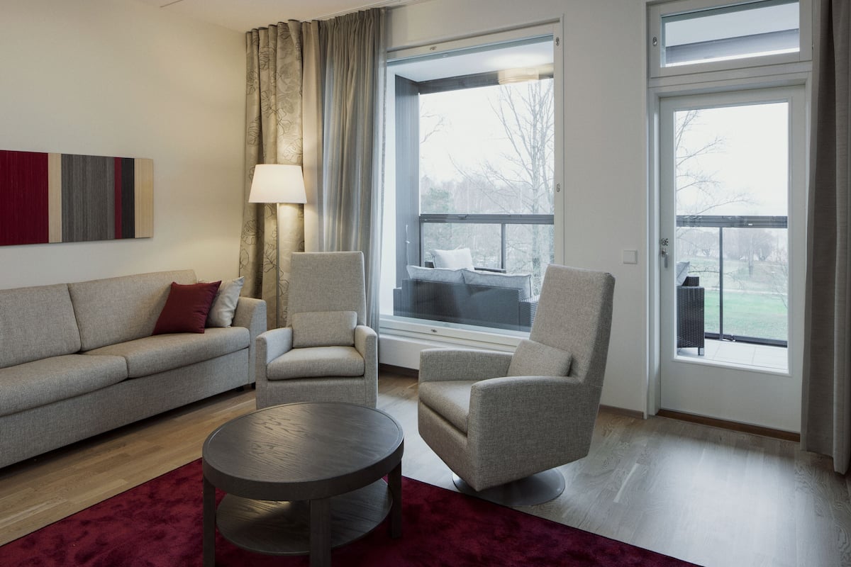 A modern living room with a sofa, two armchairs, a coffee table, and a large window with a view of the outdoors.