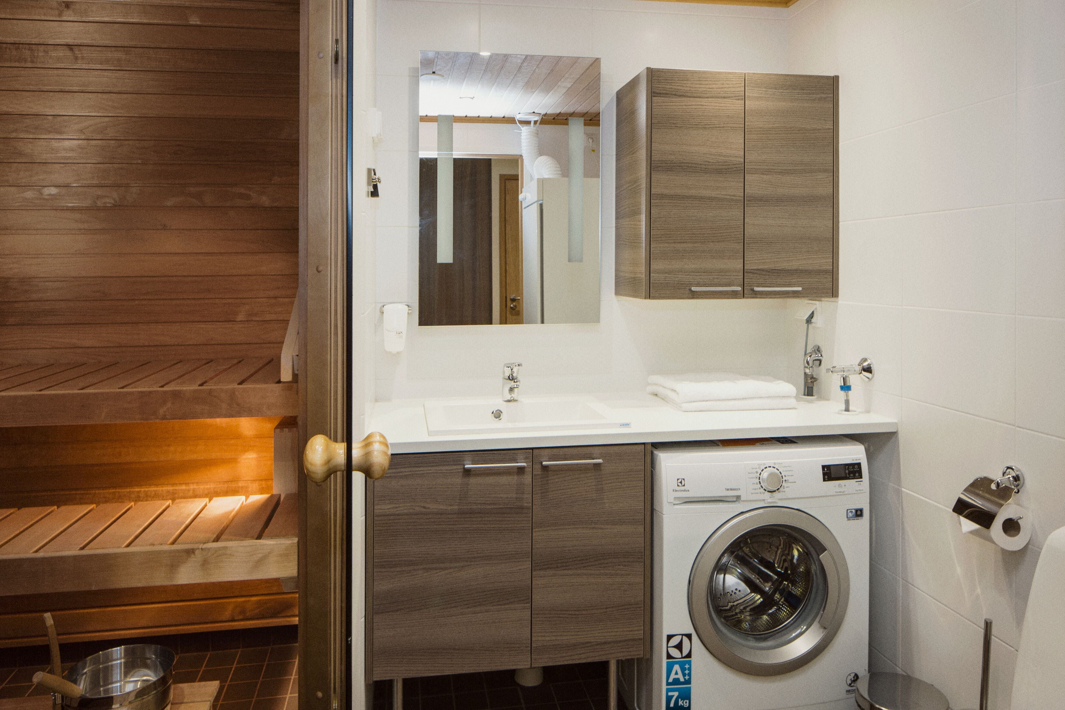Un baño moderno con un banco de madera, una lavadora, un lavamanos y un espejo.