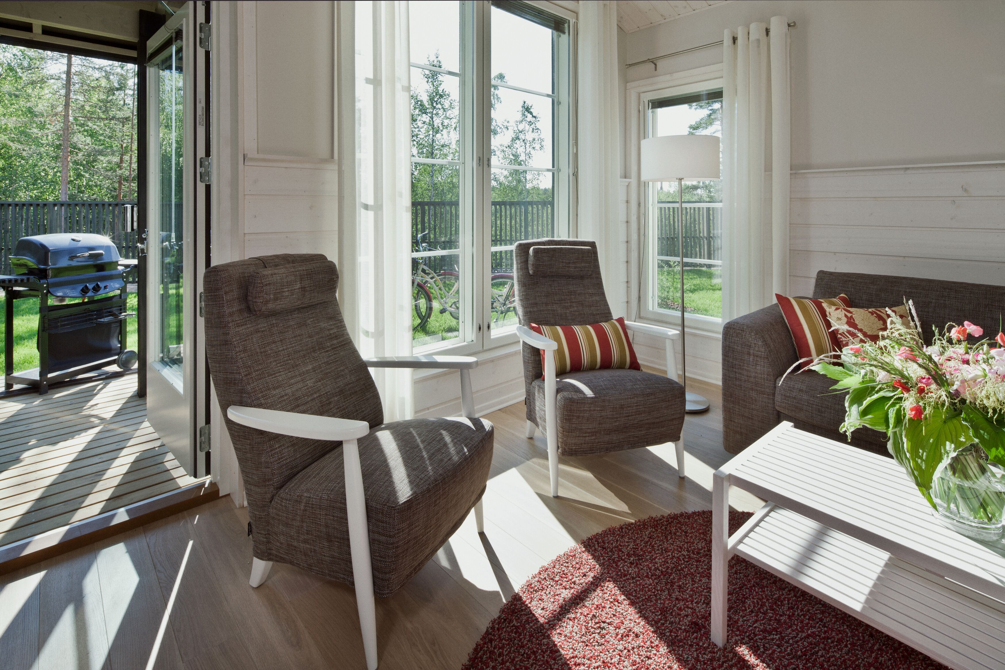 A room with a sliding glass door leading to a patio, two upholstered chairs, a white coffee table, and a floral arrangement.