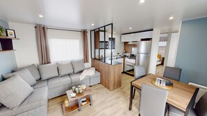 Een moderne woonkamer met een grijze bank, een houten salontafel en een eethoek met een houten tafel en stoelen.