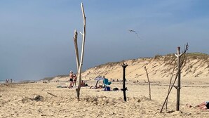 Een zanderig strand met weinig begroeiing, enkele mensen en een heldere lucht.