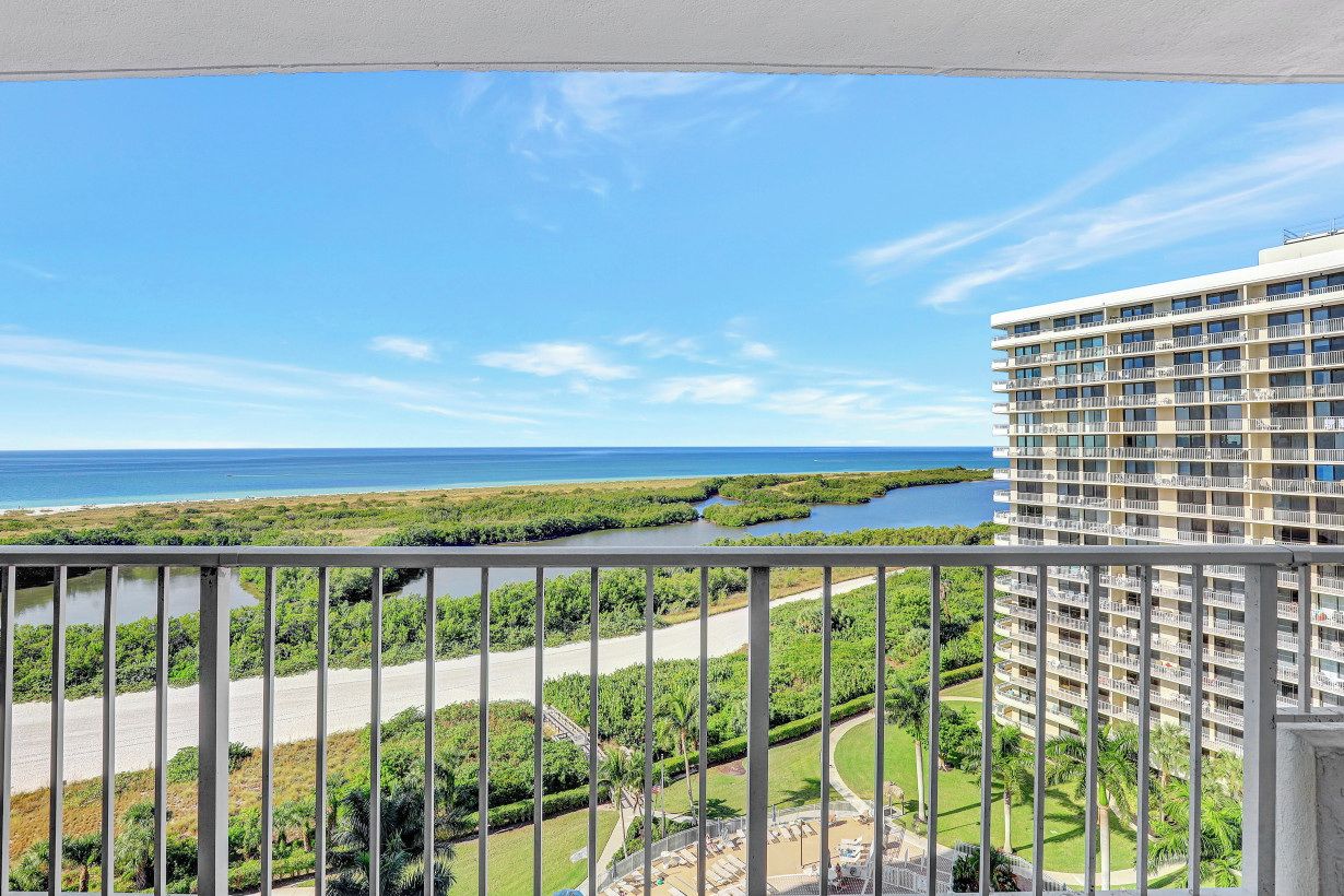 A high-rise hotel with a balcony overlooking a coastal area, including a beach and mangrove.