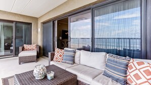 A balcony with a sofa, cushions, and a glass door leading to a room. - Oceanfront Condo with Oceanside Pool and Private Fishing Pier Access by RedAwning (Fernandina Beach)