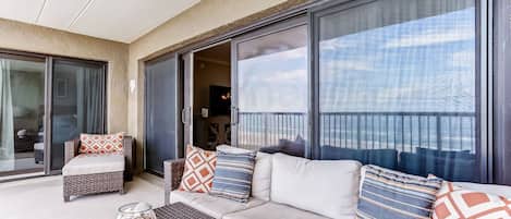 A balcony with a sofa, cushions, and a glass door leading to a room.