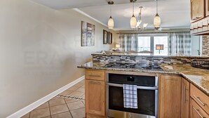 A modern kitchen with granite countertops, stainless steel appliances, wooden cabinets, and pendant lighting. - Oceanfront Condo with Oceanside Pool and Private Fishing Pier Access by RedAwning (Fernandina Beach)