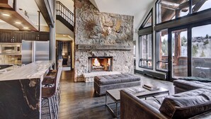 A spacious living area with a stone fireplace, a bar with stools, and a large window offering a view of the outdoors.