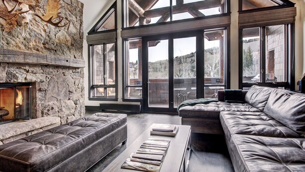 A spacious living room with a stone fireplace, leather sofas, and large windows offering a view of the outdoors.