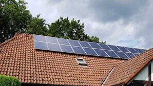 Ein Haus mit Ziegeldach, Solaranlage, einer überdachten Terrasse und einem gepflegten Rasen.