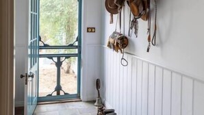 A hallway with a stone floor, a door leading outside, and a wall-mounted rack of hats and boots.