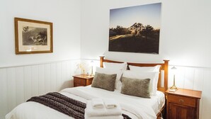A neatly made bed with a blanket and towels, a framed picture on the wall, and a landscape painting above the bed.