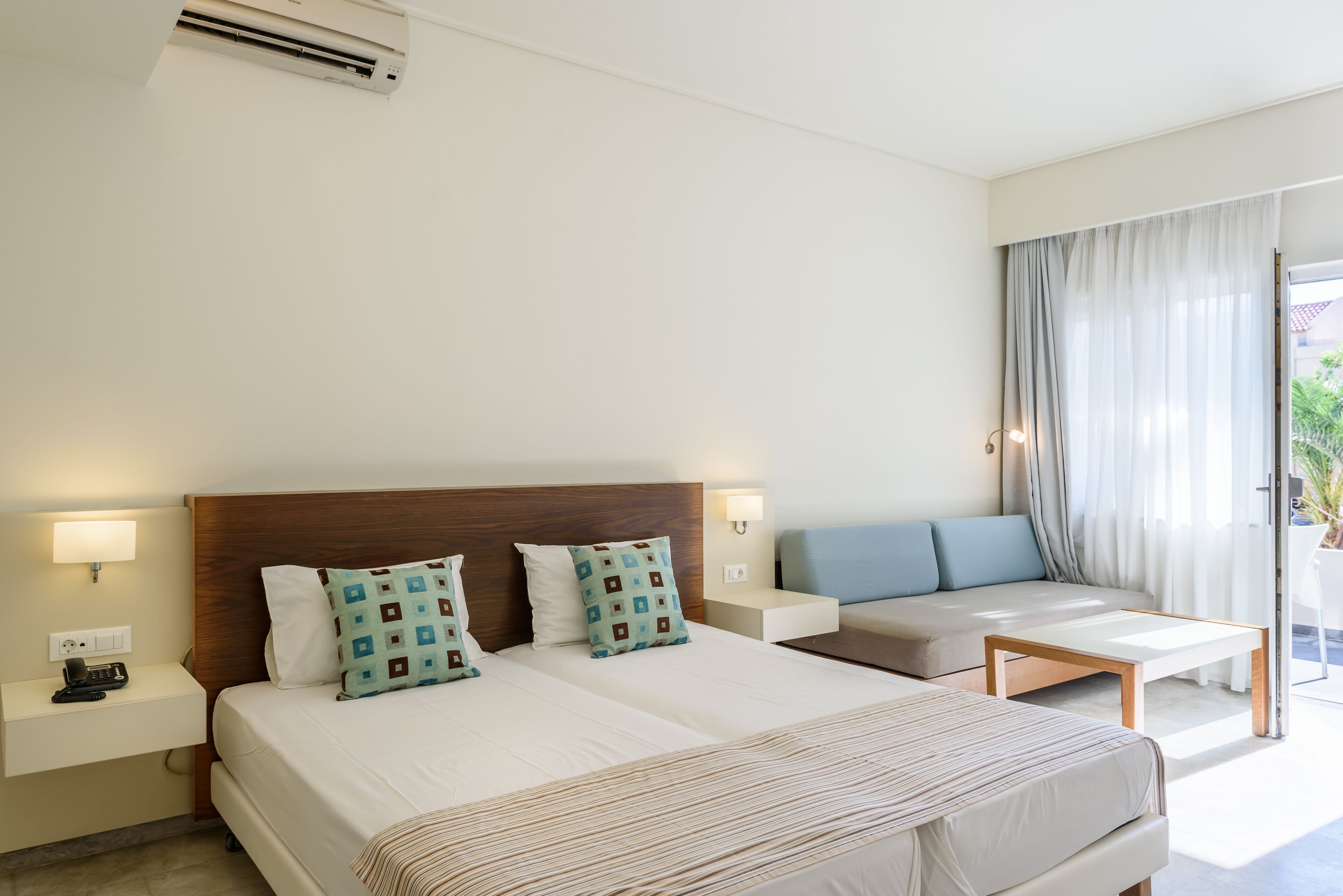 A hotel room with two beds, a sofa, a small table, and a window with curtains.