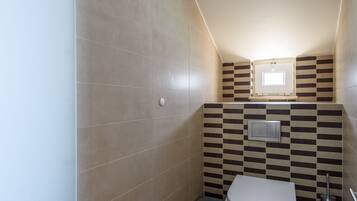 A small, modern bathroom with a toilet, a trash bin, and a wall-mounted light fixture.