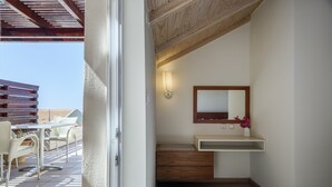 A bathroom with a wooden ceiling, a white sink, a mirror, and a small shelf with flowers.