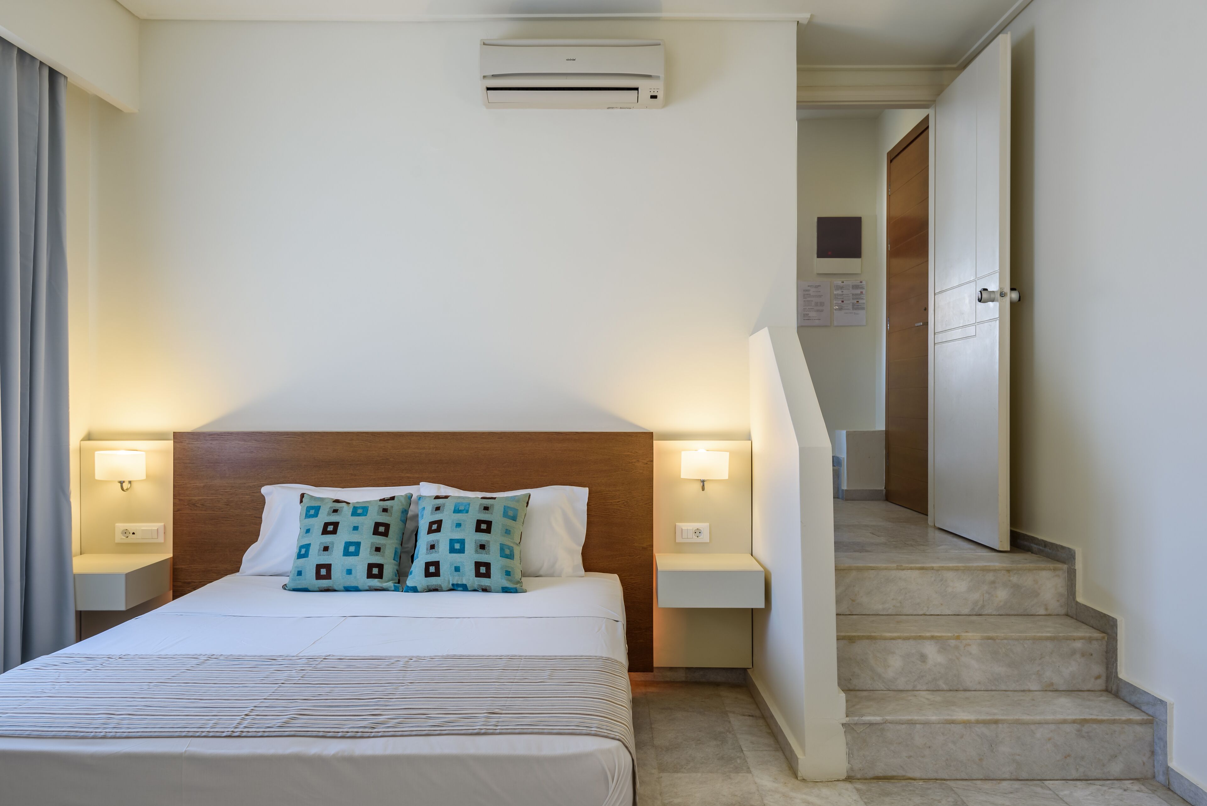 A hotel room with a bed, nightstands, a wall-mounted air conditioner, and a staircase.