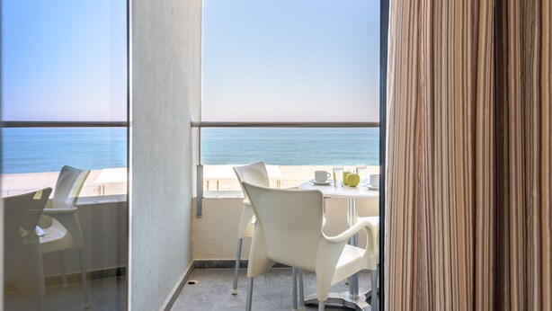 A balcony with white chairs and a table, overlooking the sea.