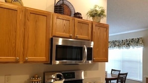 Una cocina con gabinetes de madera, un microondas de acero inoxidable, una estufa y un hervidor.
