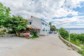 Stroll along a tranquil street lined with lush greenery and flowering plants, leading to a serene waterfront view.
