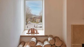 A room with a window overlooking a street, a fireplace, and a stack of firewood. - Host & Stay | The Cobbles (Osmotherley)