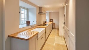 A modern kitchen with a wooden countertop, white cabinets, and a window providing natural light. - Host & Stay | The Cobbles (Osmotherley)