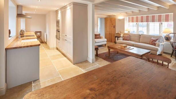 A spacious living area with a wooden dining table, a sofa, and a kitchen area with a large cabinet and a built-in oven. - Host & Stay | The Cobbles (Osmotherley)