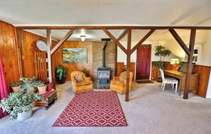 A cozy living room with wooden beams, a fireplace, two armchairs, a dining table, and various plants. - Cozy Cabin bordering Pikes National Forest  (Woodland Park)