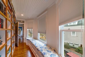 A room with a built-in bench along the window, a bookshelf, and a door leading to another room.
