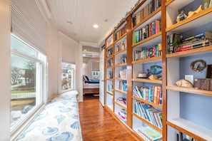 Un pasillo con una estantería de madera llena de libros, un tapete estampado y una ventana con persianas.