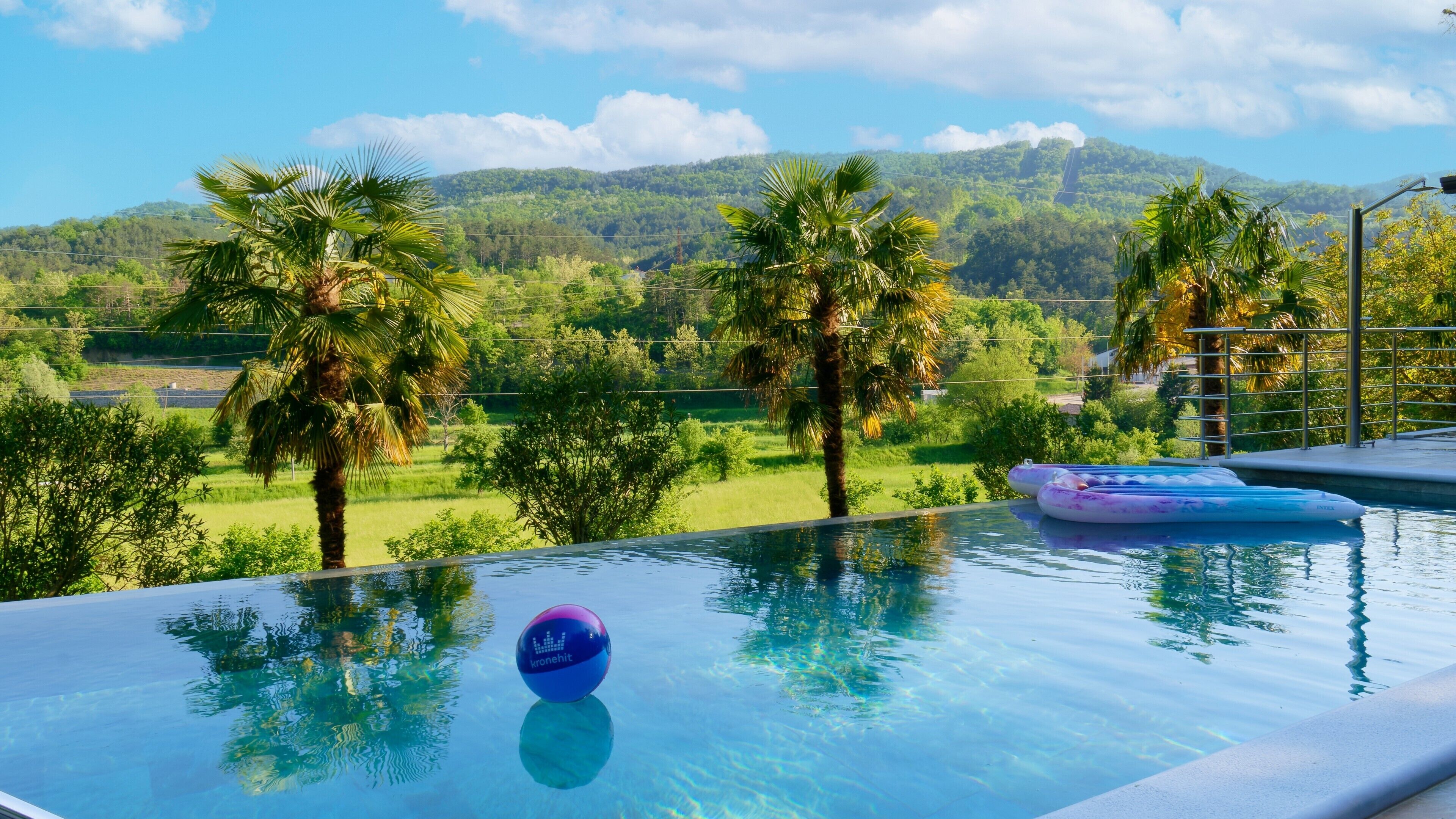 An infinity pool with a clear view of a lush landscape, including palm trees and distant hills.
