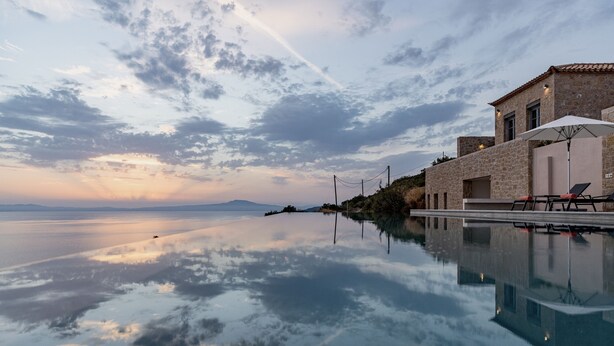 Una vista tranquila de un lago con un edificio de piedra, cielo despejado y una superficie acuática calma que refleja el entorno.