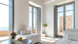 Amplia sala de estar con un sofá, una mesa redonda con una planta y libros, y grandes ventanas que ofrecen vista al mar.