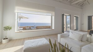 Una sala de estar moderna con un amplio ventanal con vista al mar, un sofá blanco y una pequeña planta en maceta.