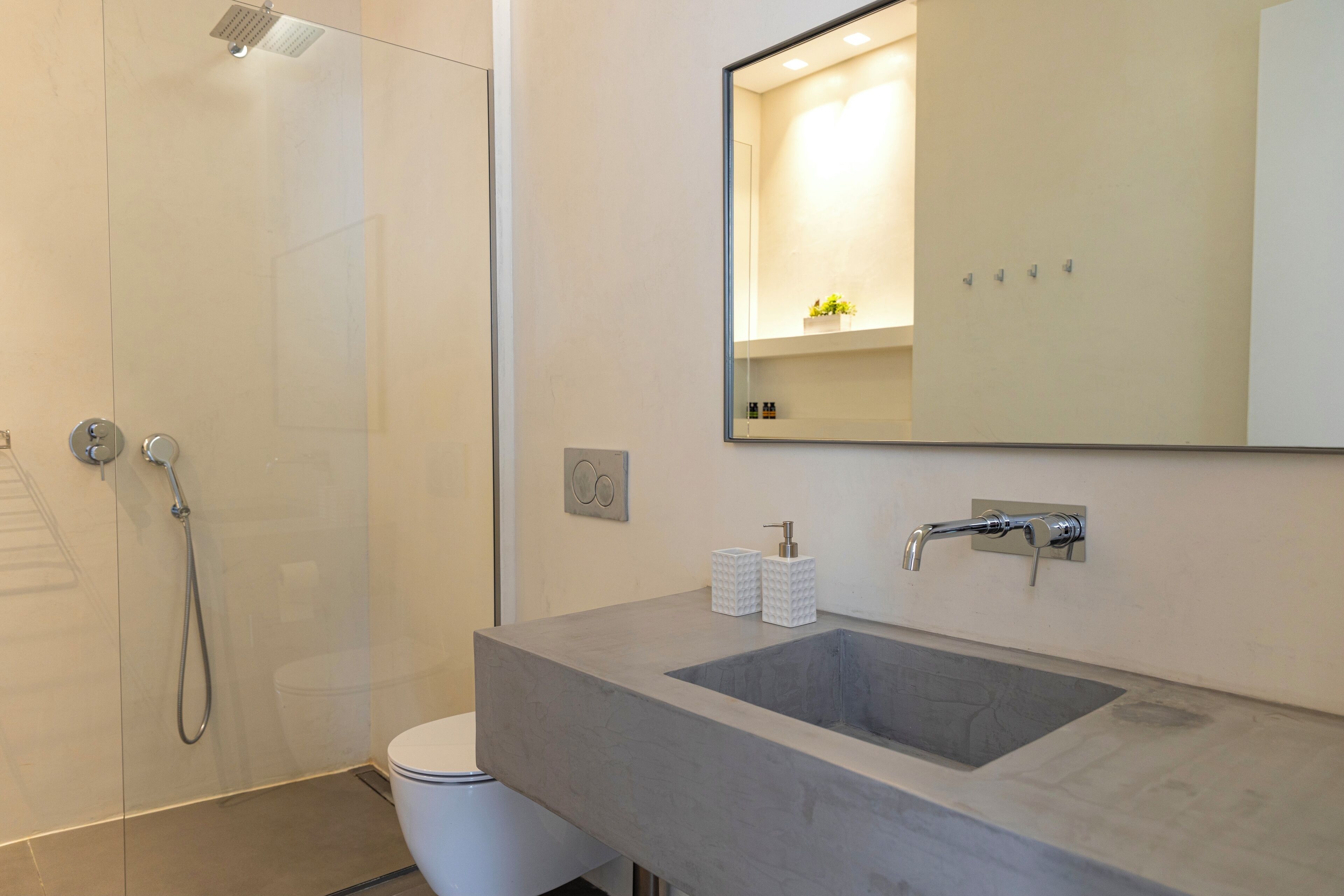 Een moderne badkamer met een douchecabine van glas, een wit toilet en een grote wastafel met een spiegel erboven.
