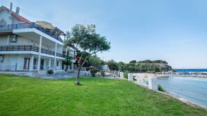 A coastal property with a large building featuring multiple balconies, a grassy lawn, and a beach with boats.