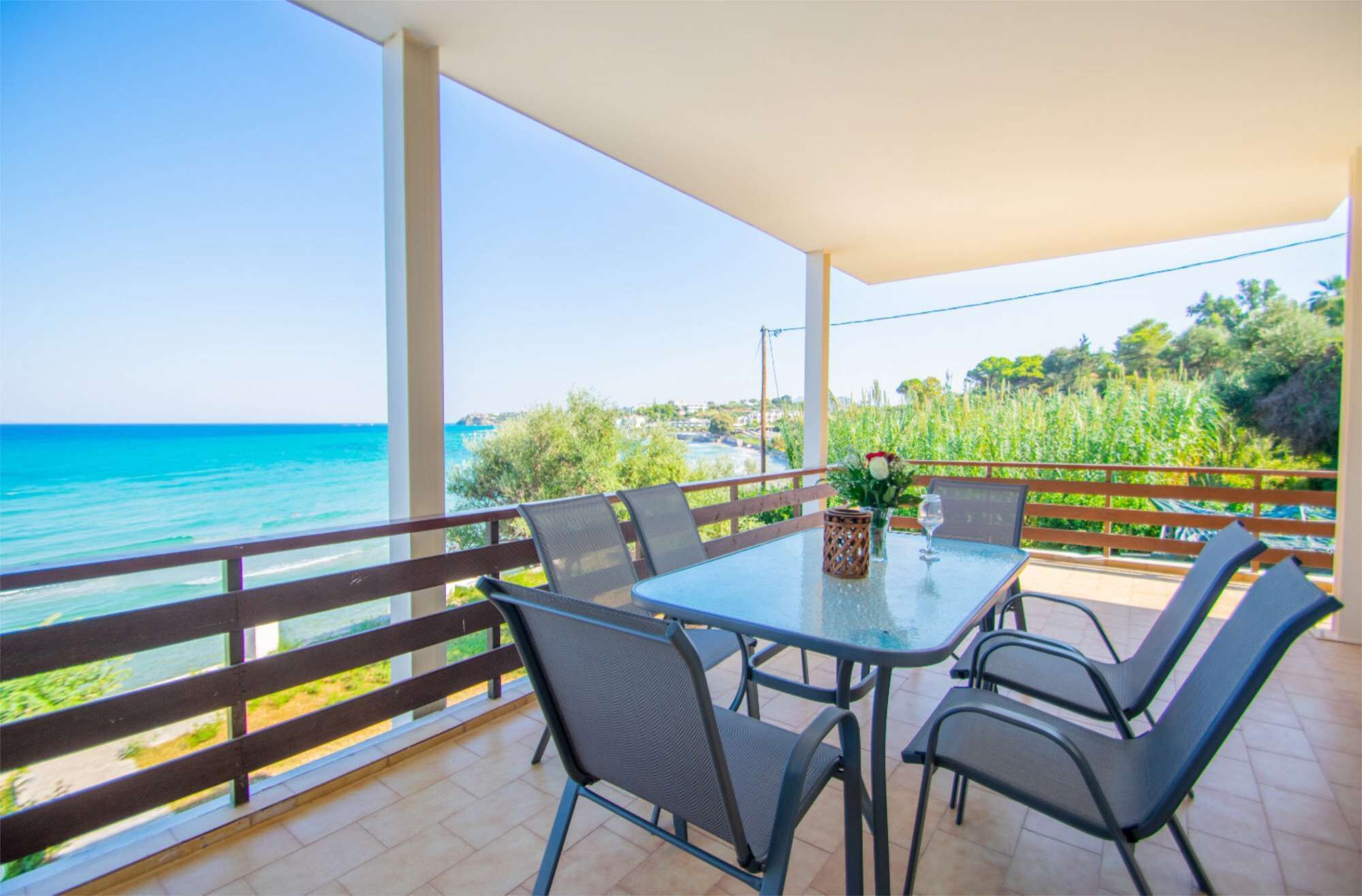A covered outdoor seating area with a table and chairs, overlooking a coastal view.