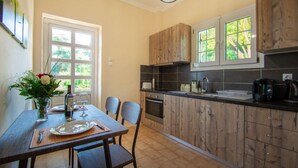 A kitchen with wooden cabinets, a dining table with chairs, a vase with flowers, and a window with a view of greenery.