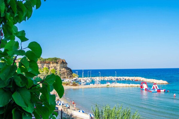 Relax on the beach with umbrellas and chairs, surrounded by lush greenery and a serene sea.
