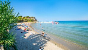 A beach with clear blue water, people sunbathing, and a rocky cliff in the background.