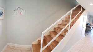 A staircase with wooden steps and white railings, a light blue wall, and a framed picture with the word "BeAC" on it.