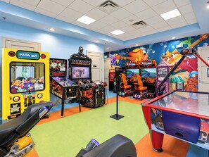 A brightly lit indoor arcade with various gaming machines, including a yellow bus-themed claw machine and multiple racing game setups.