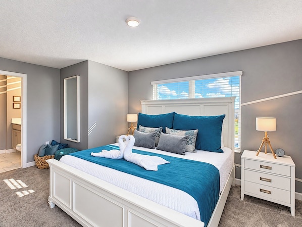 A modern bedroom with a large bed, bedside tables, a mirror, and a window with blinds.
